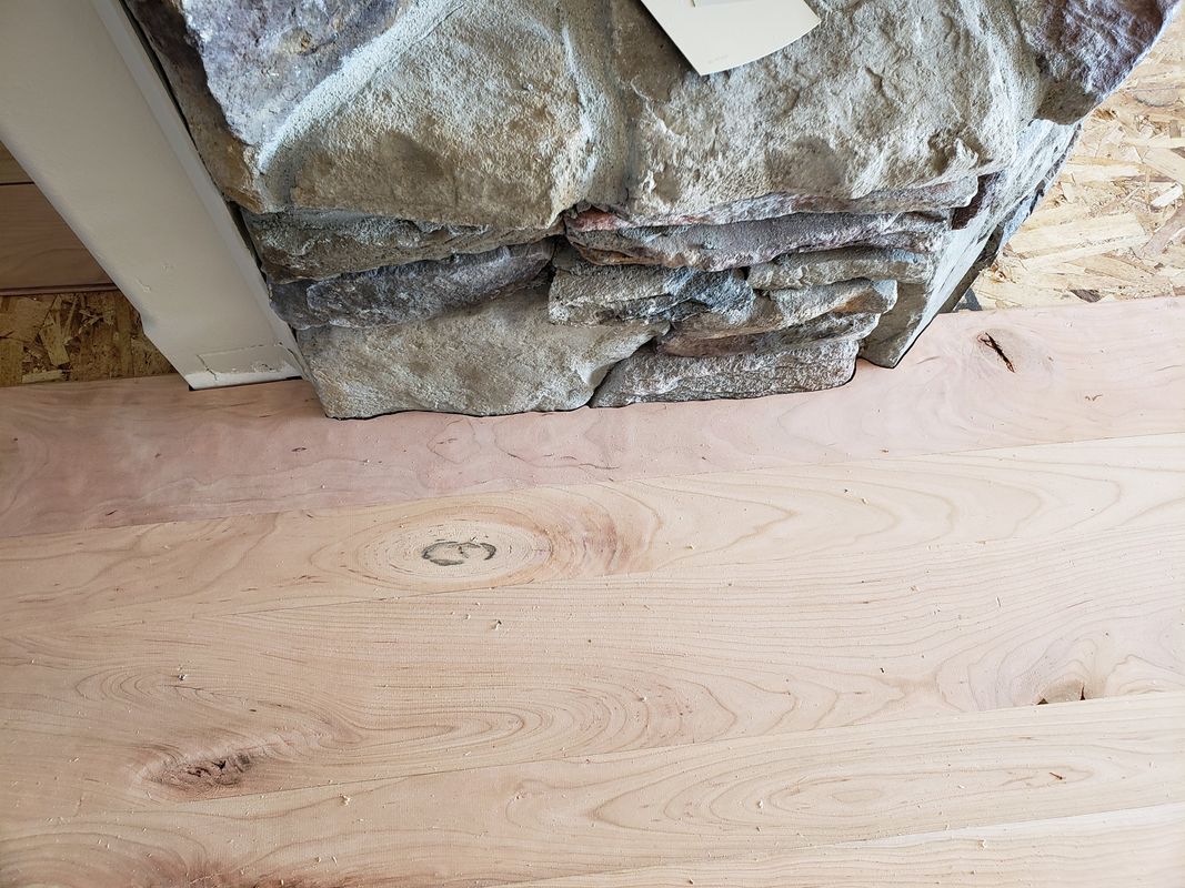 Wide-plank hardwood fitted around stone fireplace base